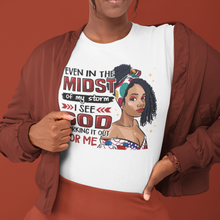 Load image into Gallery viewer, White t-shirt with a young African American black woman wearing a head band and a cross. With the words even in the midst of the storm, I see God working it out for me. Also in the picture is black shoes and blue jeans on the bottom sides.