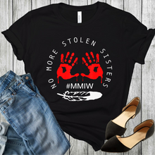 Load image into Gallery viewer, On this black t-shirt is #MMIW and the words no more stolen sisters and a feather in white. Red bloody hands in a circle. Black shoes and blue jeans in the bottom corners of the picture.