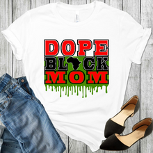 Load image into Gallery viewer, African American T-Shirt Dope Black Mom white t shirt with the words Dope &amp; Mom In red and the word Black in black and the continent Africa replaced the letter A in the word black and green drip behind the words Black &amp; Mom. Also a pair of black shoes and blue jeans in the picture.
